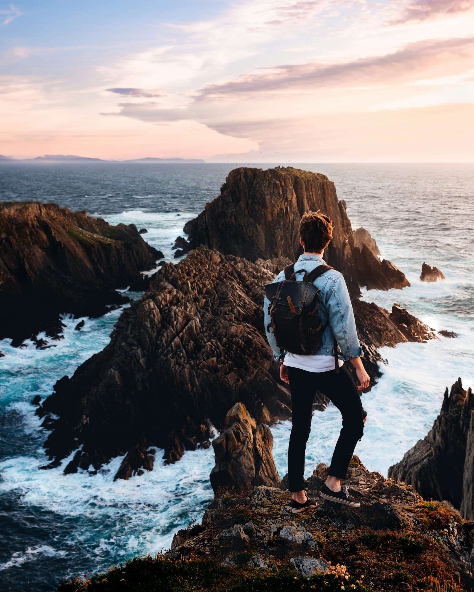 A young traveler looking out over the sea at sunset